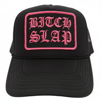 A black trucker hat with fuchsia embroidery reading 'BITCHSLAP' on the front.