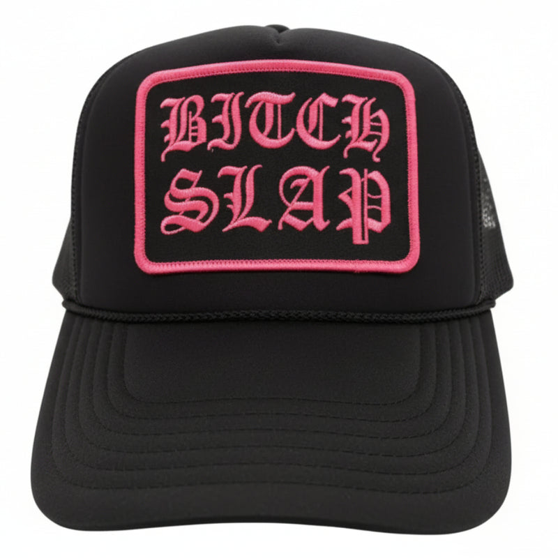 A black trucker hat with fuchsia embroidery reading 'BITCHSLAP' on the front.